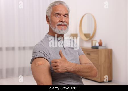 Seniorenmann mit Klebebandage am Arm nach der Impfung, mit Daumen nach oben zu Hause Stockfoto