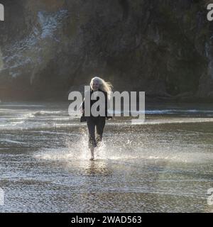 USA, Oregon, Newport, Frau, die am Sandstrand läuft und Wasser spritzt Stockfoto