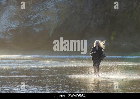 USA, Oregon, Newport, Frau, die am Sandstrand läuft und Wasser spritzt Stockfoto