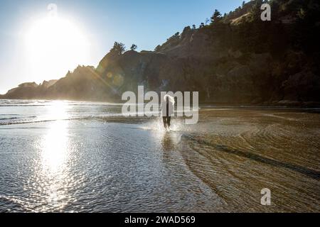 USA, Oregon, Newport, Frau, die am Sandstrand läuft und Wasser spritzt Stockfoto