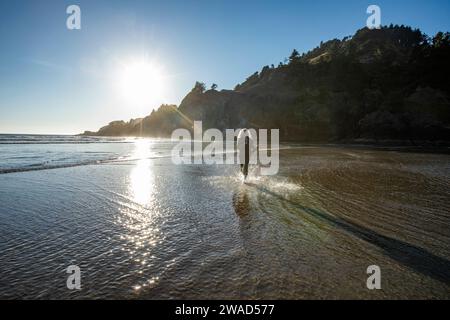 USA, Oregon, Newport, Frau, die am Sandstrand läuft und Wasser spritzt Stockfoto