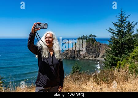 USA, Oregon, Brookings, Senior Woman macht Selfie mit Küstenlandschaft im Hintergrund Stockfoto