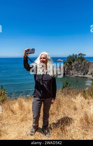 USA, Oregon, Brookings, Senior Woman macht Selfie mit Küstenlandschaft im Hintergrund Stockfoto