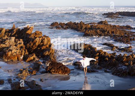 Südafrika, Hermanus, Junge (10-11), der zwischen Felsen am Kammabaai Beach läuft Stockfoto