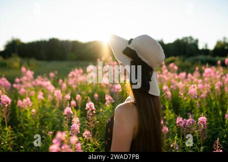 Junge Frau mit Strohhut, die auf der Wiese steht, an sonnigem Tag Stockfoto