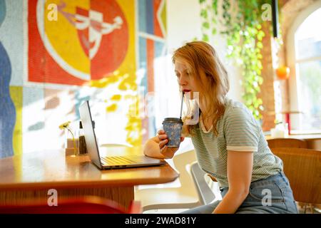 Seitenansicht einer Frau, die am Laptop arbeitet, während sie Kaffee im Café trinkt Stockfoto
