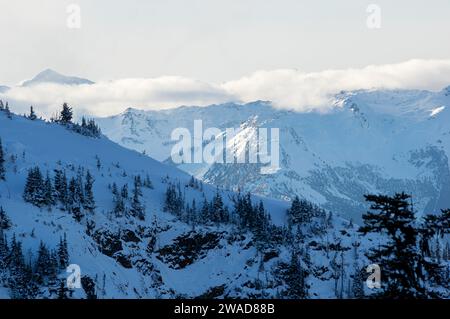 Ein dramatischer Blick auf schneebedeckte Gipfel, die von Wolken umgeben sind, umgeben von felsigen zerklüfteten Bergrücken und Hängen vom Whistler Mountain, BC, Kanada. Stockfoto