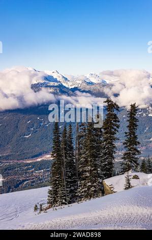 Ein Blick auf die Schneekappen der Berge, die von Wolken umgeben sind, mit dem Vallée in der Ferne und Bäumen und eine Skipiste im Vordergrund vom Blackcomb Mountain in W Stockfoto