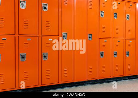 Orangefarbene Metallschränke entlang eines unscheinbaren Flurs an einer typischen US-High School. Keine identifizierbaren Informationen enthalten und niemand in der Halle. Stockfoto