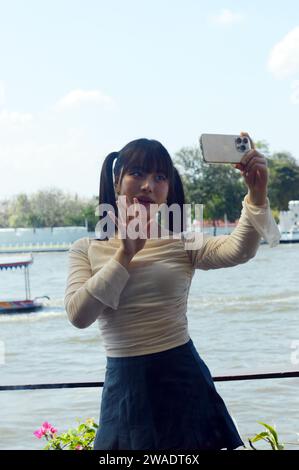 Eine Frau von Gen Z posiert für Selfies und Vlogs für ihre sozialen Medien am Fluss Chao phraya in Bangkok, Thailand Stockfoto