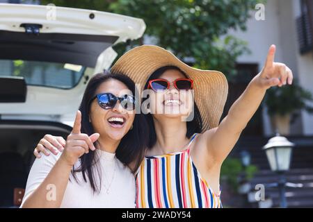 Glückliche asiatische Freundinnen, die ihr Gepäck im Auto packen und sich zu Hause im Garten umarmen. Leben im Haushalt, Sommer, Freundschaft, Reisen und Lebensstil, unveränderlich. Stockfoto