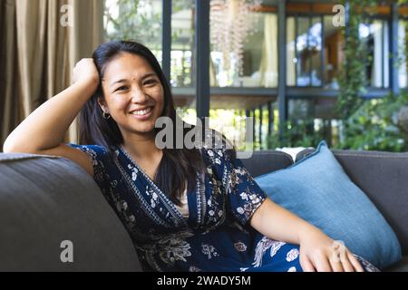 Porträt einer glücklichen asiatischen Frau, die zu Hause auf der Couch sitzt. Leben und Lebensstil unverändert. Stockfoto
