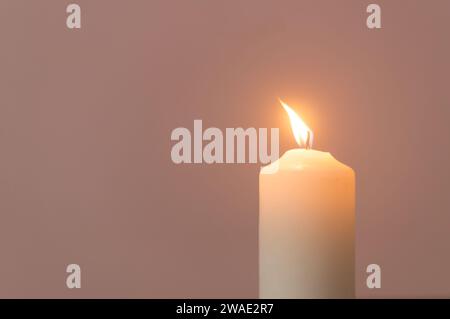 Verschwommenes Foto von einer einzelnen brennenden Kerzenflamme oder Licht leuchtet auf einer weißen Kerze auf cremefarbenem Hintergrund auf Tisch in der Kirche für Weihnachten, Beerdigung Stockfoto