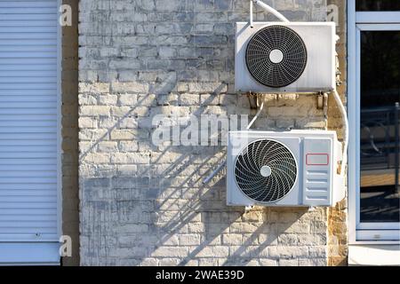 Externe Klimaanlagen an einer alten Ziegelwand mit einem Bruchstück eines Metall-Kunststoff-Fensters und Metalljalousien. Stockfoto