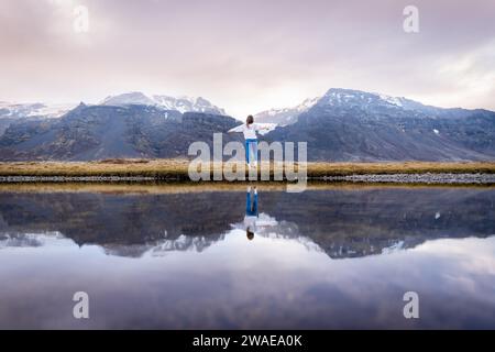 Eine Frau steht auf einem üppigen, grasbewachsenen Hügel mit Blick auf einen ruhigen See Stockfoto