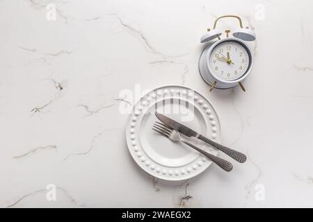 Konzept des intermittierenden Fasten, leere Platte mit Uhr auf weiß Stockfoto