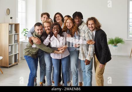 Porträt fröhlicher multirassischer Kollegen im Amt, die sich umarmen, um Einheit und Unterstützung bei der Arbeit zu zeigen. Stockfoto