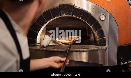 Koch schiebt Pizza in einen modernen Holzofen Stockfoto