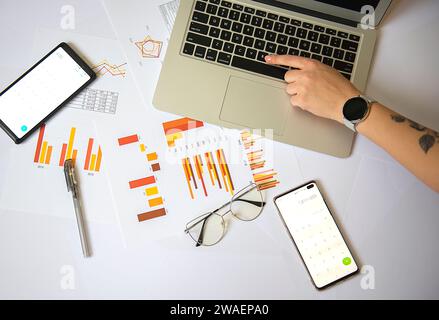 Eine Person, die auf einem Laptop an einem Schreibtisch mit Smartphone und Dokumenten schreibt Stockfoto