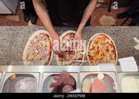 Koch bei der Arbeit: Basteln Sie Pizzen mit verschiedenen Belägen Stockfoto