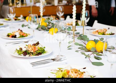 Ein elegant gedeckter Esstisch mit Gourmet-Salaten, mit feinem Besteck, Besteck und geschmackvoller Dekoration, bereit für eine raffinierte Mahlzeit. Stockfoto