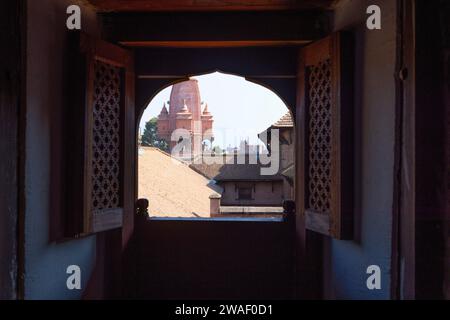 Mädchen beobachten draußen durch das Newar-Fenster mit Blick auf den Tempel von Silu Mahadeva auf dem Bhaktapur Durbar Platz Stockfoto