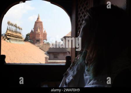 Mädchen beobachten draußen durch das Newar-Fenster mit Blick auf den Tempel von Silu Mahadeva auf dem Bhaktapur Durbar Platz Stockfoto