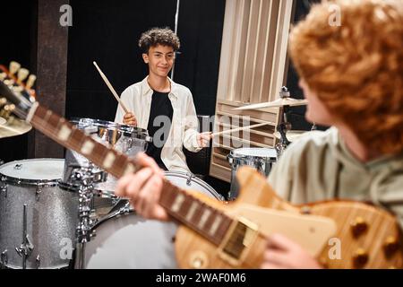 Konzentrieren Sie sich auf den fröhlichen Teenager, der Schlagzeug spielt und seinen rothaarigen, verschwommenen Freund, die Musikgruppe, ansieht Stockfoto