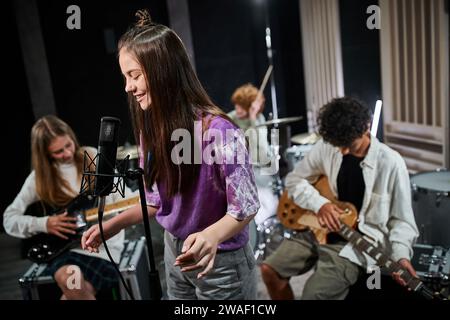 Konzentriere dich auf fröhliche Teenager-Mädchen, die singen, während ihr Freund verschiedene Instrumente spielt, Musikgruppe Stockfoto