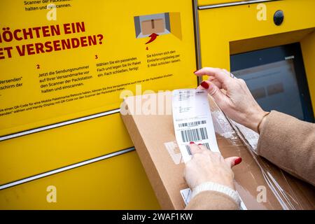 Innovative Paketlogistik - Nutzung der DHL Packstation 04.01.2024, Bad Camberg: Symbolfoto, Illustrationsbild, Symbolbild, Illustrationsfoto das Bild zeigt eine Frau im Anschnitt, die mit ihrem Smartphone über den Touchscreen einer DHL Paketstation interagiert, um ein Paket einzureichen. Sie ist konzentriert auf die digitale Schnittstelle fokussiert, während Ihre Hand das Mobiltelefon hält und die entsprechenden Eingaben auf dem Bildschirm der Paketstation tätigt um das Paket einlegen. Die Packstation, ein Paketautomatensystem von DHL, bietet seit 2001 in über 12,500 Standorten deutschlandwe Stockfoto