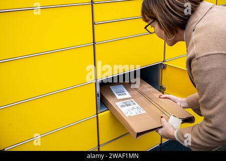 Innovative Paketlogistik - Nutzung der DHL Packstation 04.01.2024, Bad Camberg: Symbolfoto, Illustrationsbild, Symbolbild, Illustrationsfoto das Bild zeigt eine Frau im Anschnitt, die mit ihrem Smartphone über den Touchscreen einer DHL Paketstation interagiert, um ein Paket einzureichen. Sie ist konzentriert auf die digitale Schnittstelle fokussiert, während Ihre Hand das Mobiltelefon hält und die entsprechenden Eingaben auf dem Bildschirm der Paketstation tätigt um das Paket einlegen. Die Packstation, ein Paketautomatensystem von DHL, bietet seit 2001 in über 12,500 Standorten deutschlandwe Stockfoto