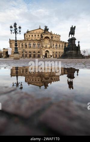 Dresden, Deutschland. Januar 2024. Die Semperoper und die Reiterstatue von König John spiegeln sich am Morgen in einer Pfütze auf dem Theaterplatz wider. Robert Michael/dpa/Alamy Live News Stockfoto