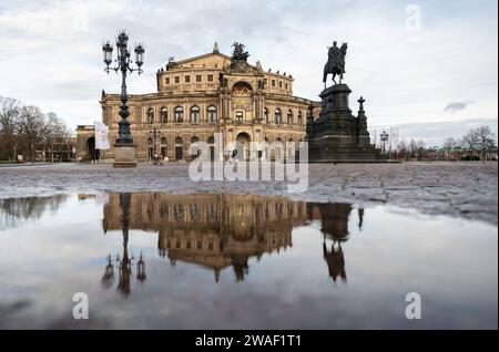 Dresden, Deutschland. Januar 2024. Die Semperoper und die Reiterstatue von König John spiegeln sich am Morgen in einer Pfütze auf dem Theaterplatz wider. Robert Michael/dpa/Alamy Live News Stockfoto