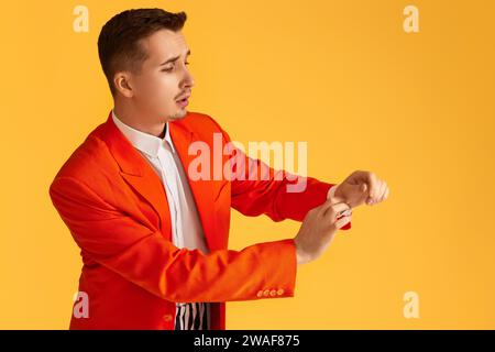 Modischer junger Mann in orangefarbener Jacke und gestreifter Hose auf gelbem Hintergrund. Stockfoto