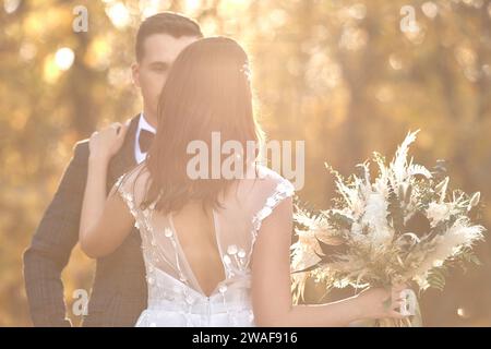 Schöne Braut in weißem Hochzeitskleid und Bräutigam, die im Freien auf natürlichem Hintergrund an sonnigem Tag stehen. Kopierbereich Stockfoto