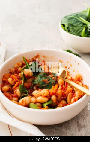 Gesundes Frühstück und Mittagessen, gedünstete weiße Bohnen mit Karotten, Zwiebeln und Tomaten mit Spinatblättern, eine Schüssel Bohnen und Spinat Stockfoto