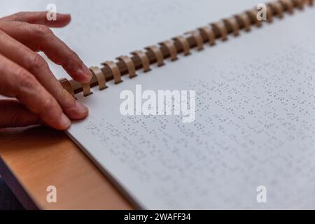 Blinde oder sehbehinderte Person, die ein Buch liest, das mit brailleschrift gedruckt ist. Stockfoto