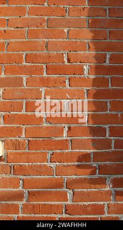 Vertikaler Hintergrund einer roten Ziegelwand in natürlichem Sonnenlicht rechts beschattet, Ziegelsteinstruktur aus orangen rechteckigen Blöcken mit weißem Zementverbinder Stockfoto