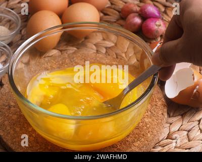 Die Eier in einer Glasschüssel mit einer Gabel von Hand mischen, als Hintergrundeier, rote Zwiebeln, Salz und Paprika verwenden Stockfoto