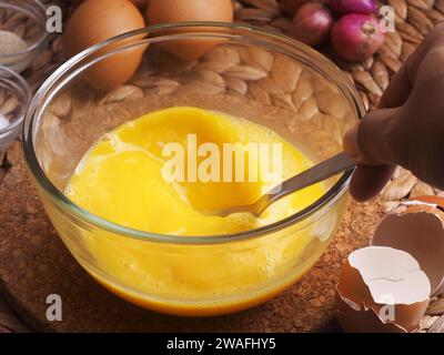 Die Eier in einer Glasschüssel mit einer Gabel von Hand mischen, als Hintergrundeier, rote Zwiebeln, Salz und Paprika verwenden Stockfoto