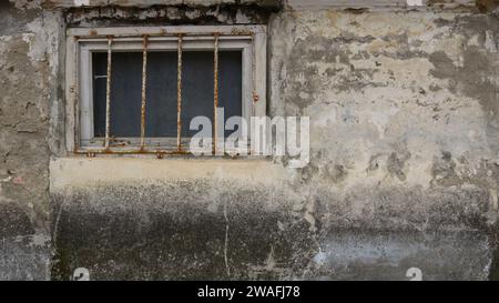 Gitterfenster auf einer schäbigen, dreckigen Wand mit einem rauen, düsteren Hintergrund, Teil der Wand eines schrecklichen Gebäudes mit einem Fenster mit Eisenstangen Stockfoto
