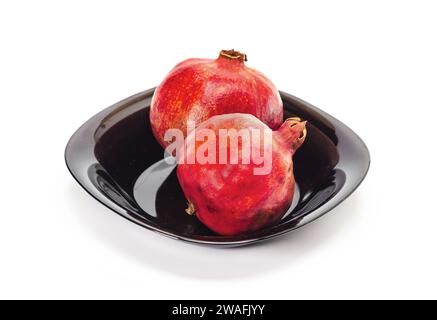 Zwei reife rote Granatäpfel in schwarzer Schüssel, isoliert auf weißem Hintergrund. Saftige Früchte. Stockfoto