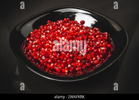 Reife rote Granatapfelkerne in schwarzer Schüssel. Dunkler Hintergrund. Nützliche Früchte für die Gesundheit. Stockfoto