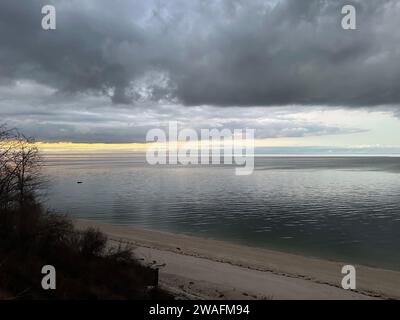 Eine ruhige Strandszene an einem bewölkten Tag mit sanft rollenden Wellen und dunklen Wolken am Himmel Stockfoto