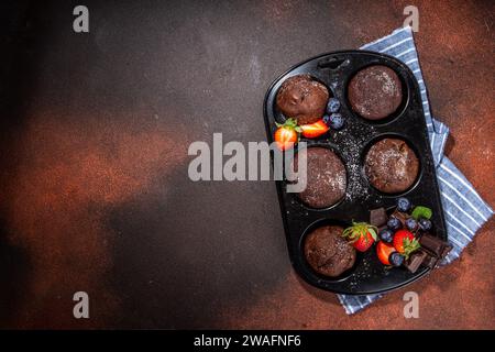 Schokoladen-Muffins mit Beeren. Muffin-Pfanne mit hausgemachten süßen, dunklen Schokoladen-Cupcakes mit Kakaosoße, Zuckerpulver und frischen Erdbeeren, Blaubeeren Stockfoto