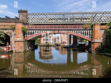 Ein Zug über eine viktorianische Eisenbahnviaduktbrücke über den Bridgewater Canal in Manchester. Viktorianische Eisenbahnbrücke, die sich im Kanal spiegelt. Stockfoto