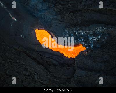 Kochendes rotes, heißes Magma, das schnell durch Lavaröhren unter einer Schicht aus schwarzer, gekühlter Lava fließt, direkt über der Luft. Konzept der Vulkanlandschaft. Stockfoto