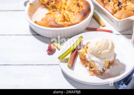 Süße Rhabarberbeerkuchen, selbstgemachter Schwammkuchen mit Rhabarber und Erdbeere, serviert mit Vanille-Eiskugel, auf sonnigen weißen Holzkrem Stockfoto