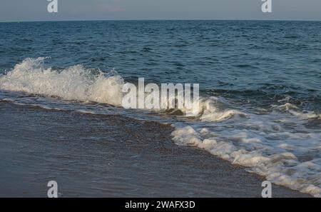 Eine große und starke Sturmwelle in türkisfarbener Farbe mit Spritzer von weißem Schaum läuft und bricht am Ufer. Stockfoto