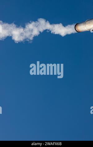 Eine Rauchfahne oder Dampf aus einem industriellen Schornstein an einem klaren blauen Himmel. Stockfoto